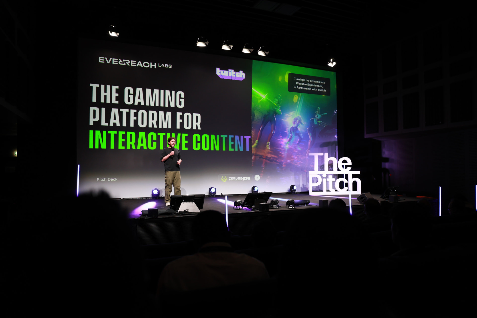 Founder pitching on stage at The Pitch Paris Edition, with an illuminated The Pitch sign and the live pitch deck on screen